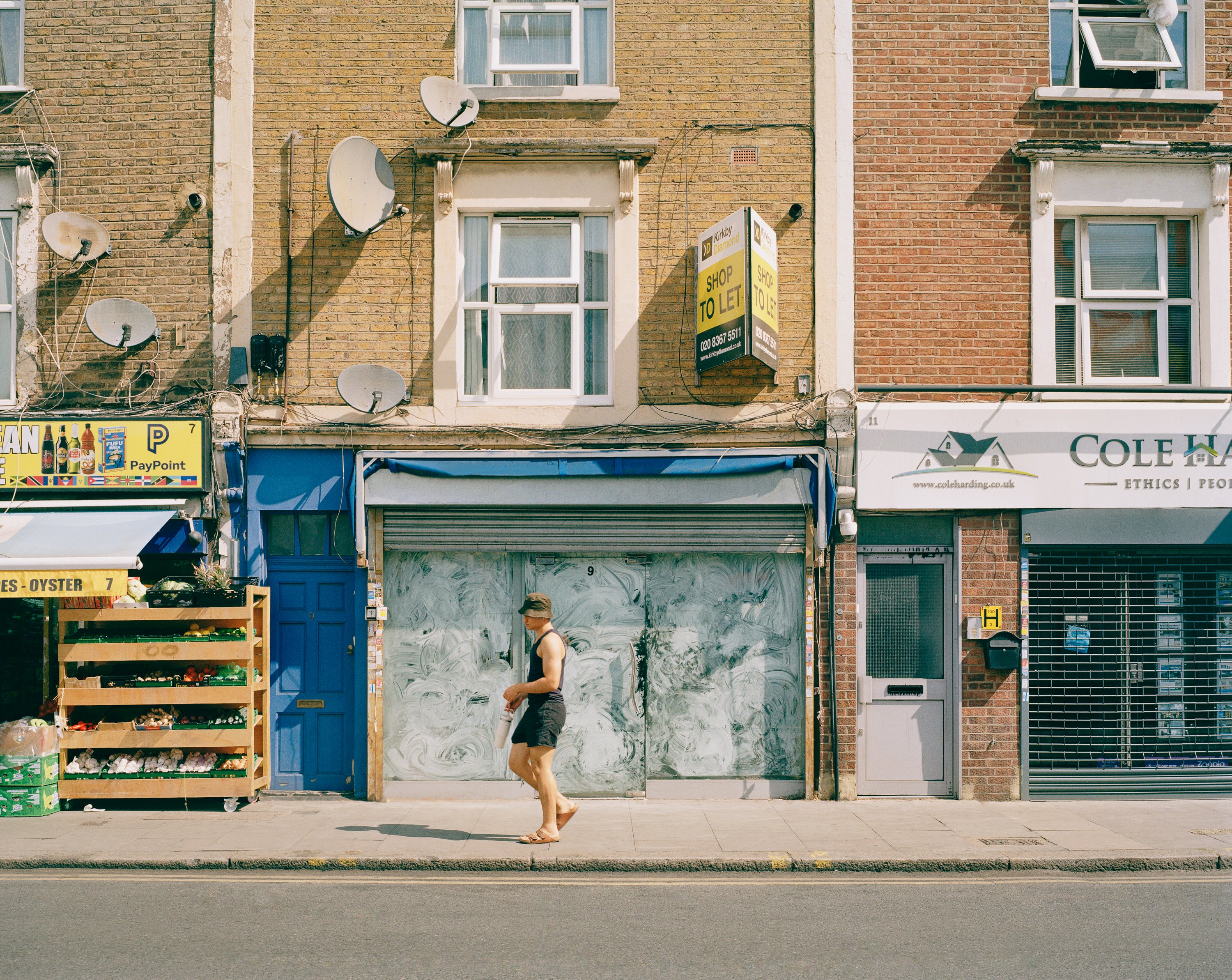 Man walking down street on a summers day past a closed down business with a to let sign.