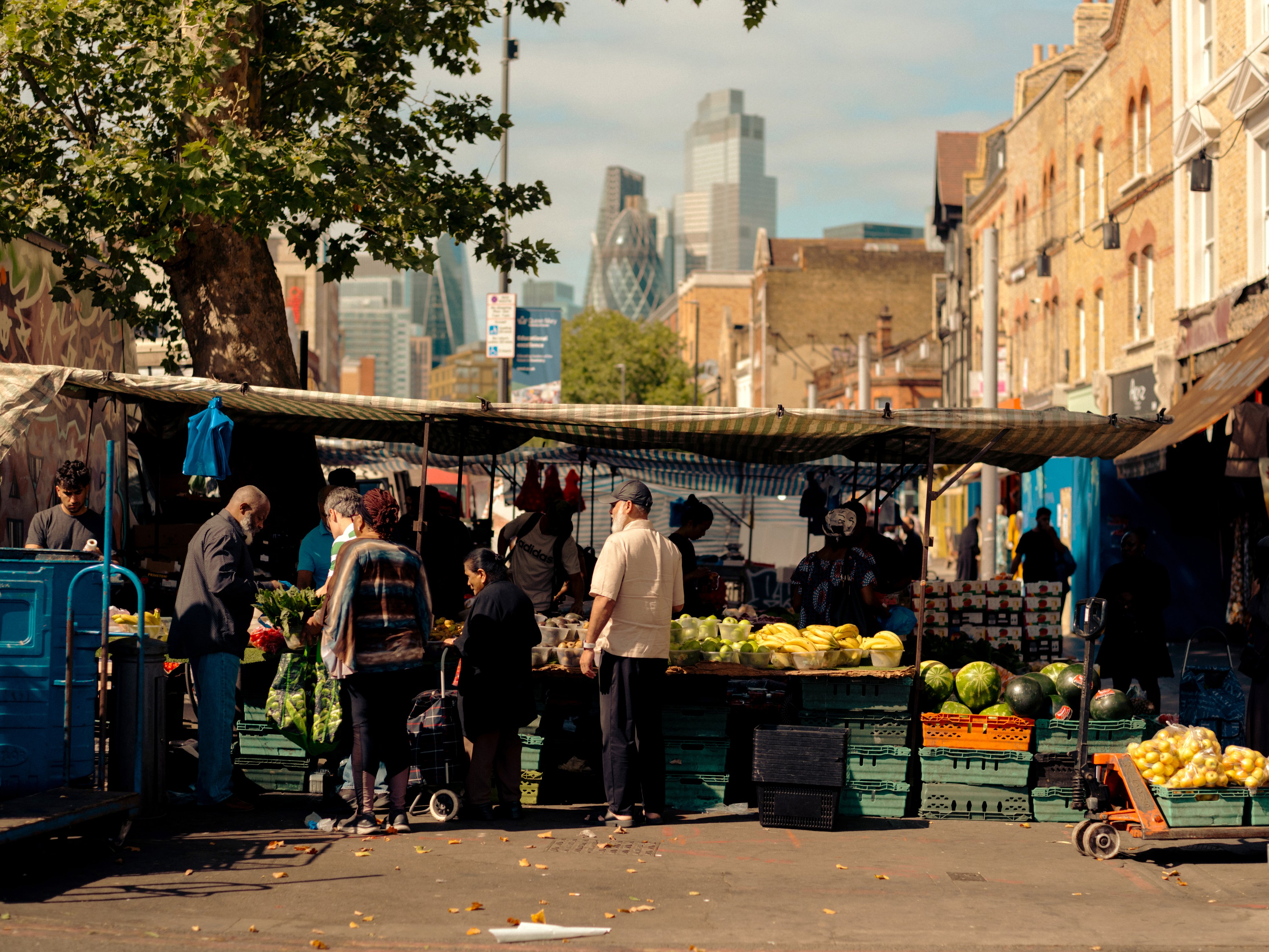 Fruit and veg market stall in foreground, London City skyline in background.