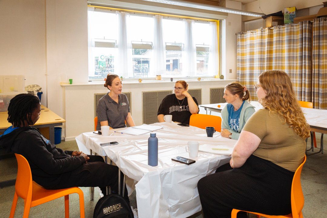 A group of 5 people in their 30s/40s sit round a table in a community centre discussing employment.