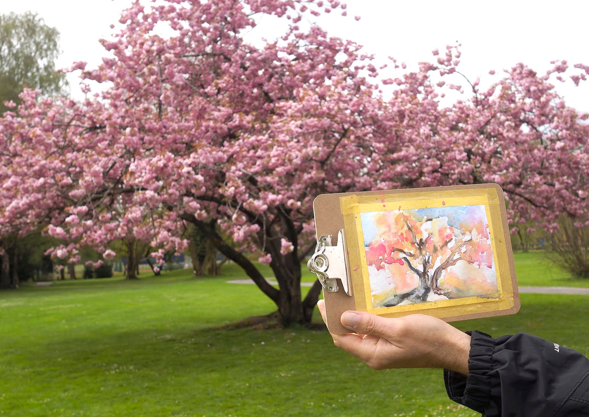Aquarell Pocket Box auf einer Bank am See mit Bergpanorama, daneben ein angefangenes Aquarellbild einer Schweizer Landschaft
