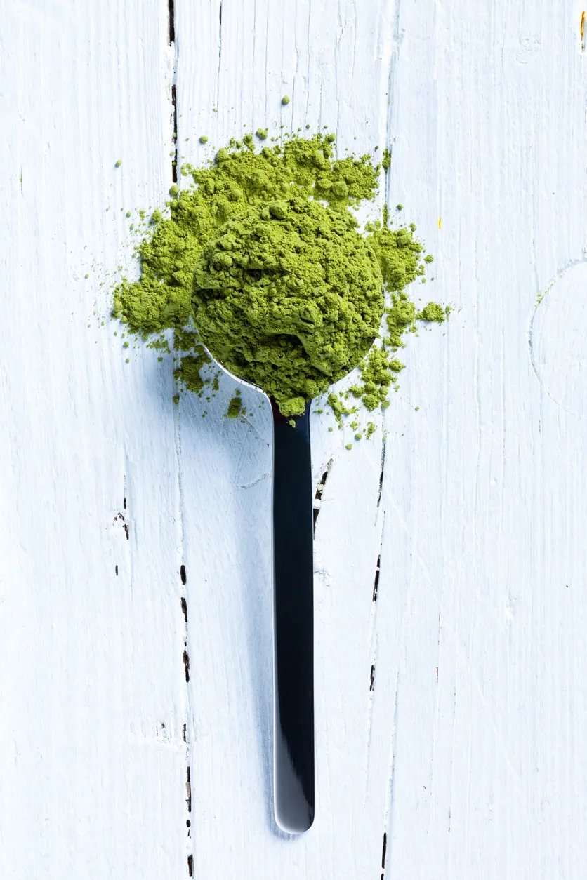 Spoonful of green EGCG powder on a white wooden surface.
