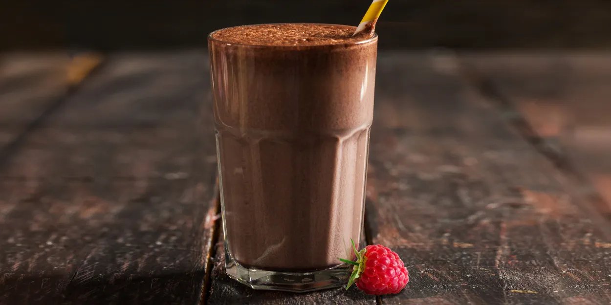 A tall glass with a chocolate raspberry shake and a fresh raspberry on a wood table