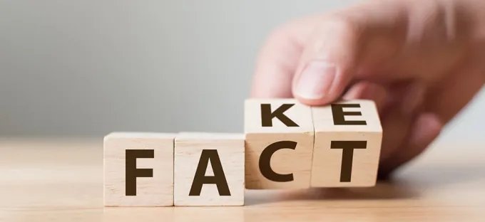 Wooden blocks spelling “FACT” or "FAKE" on a table, with a hand placing the final block.