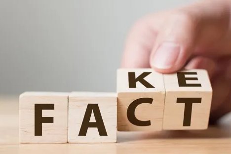 Wooden blocks spelling “FACT” or "FAKE" on a table, with a hand placing the final block.