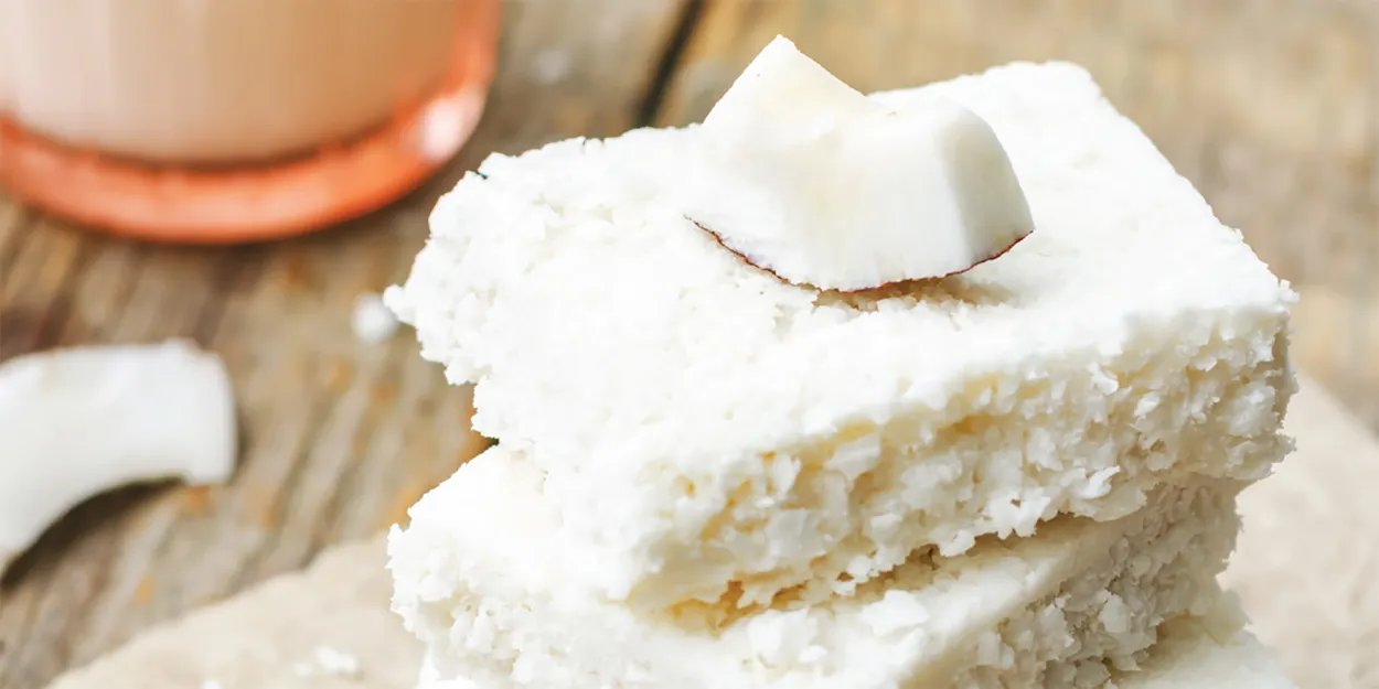 Two coconut blondies stacked with chunks of fresh coconut on a wooden table