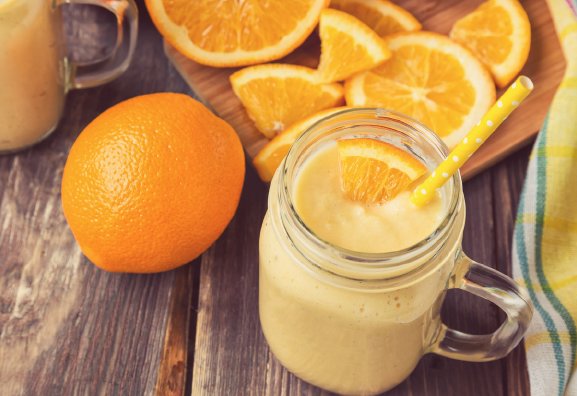 A closeup of a glass with an orange colored smoothie garnished with orange slices