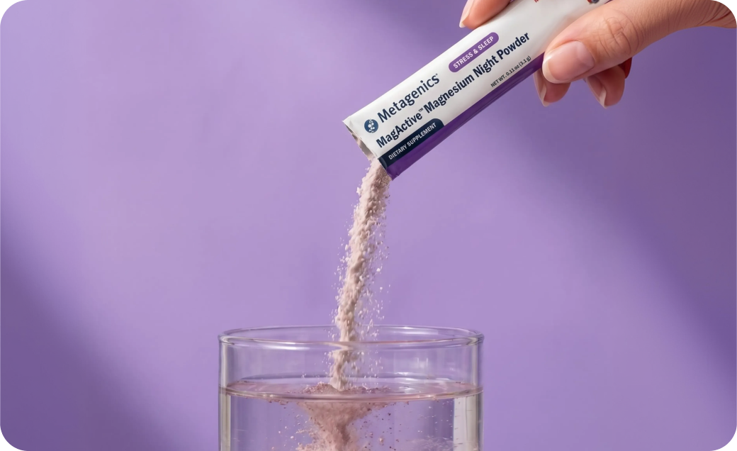 Hand pouring Metagenics MagActive® Magnesium Night Powder from a single-serve packet into a glass of water. The powder dissolves into a pink drink against a soft purple background, representing sleep and circadian support.