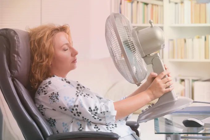 Woman experiencing a hot flash while using a fan at her desk
