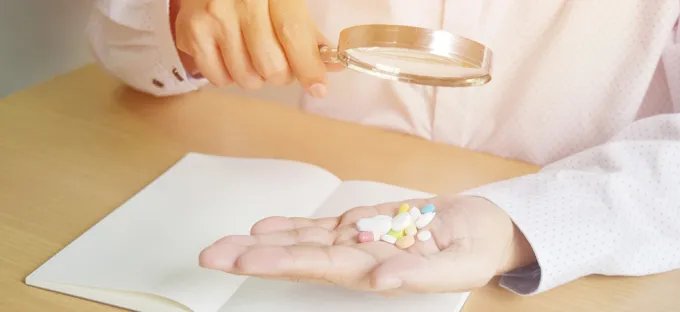 A person examining a handful of pills with a magnifying glass