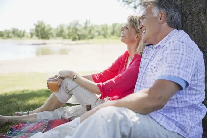 Smiling couple relaxing together on a picnic blanket beside a lake under a tree.