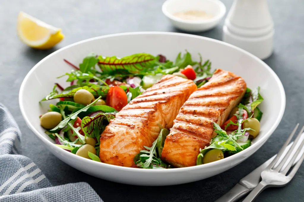 Grilled salmon fillets on a fresh salad with arugula, olives, and tomatoes — HDL-boosting foods rich in omega-3s and healthy fats
