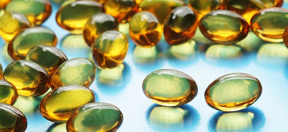 Amber-colored softgel capsules containing dietary supplements, scattered on a reflective blue surface.