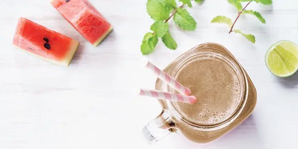 Overhead image of a watermelon smoothie in a glass with slices of watermelon, lime and mint sprigs