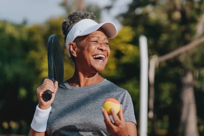 A senior African American woman smiling while playing pickle ball.