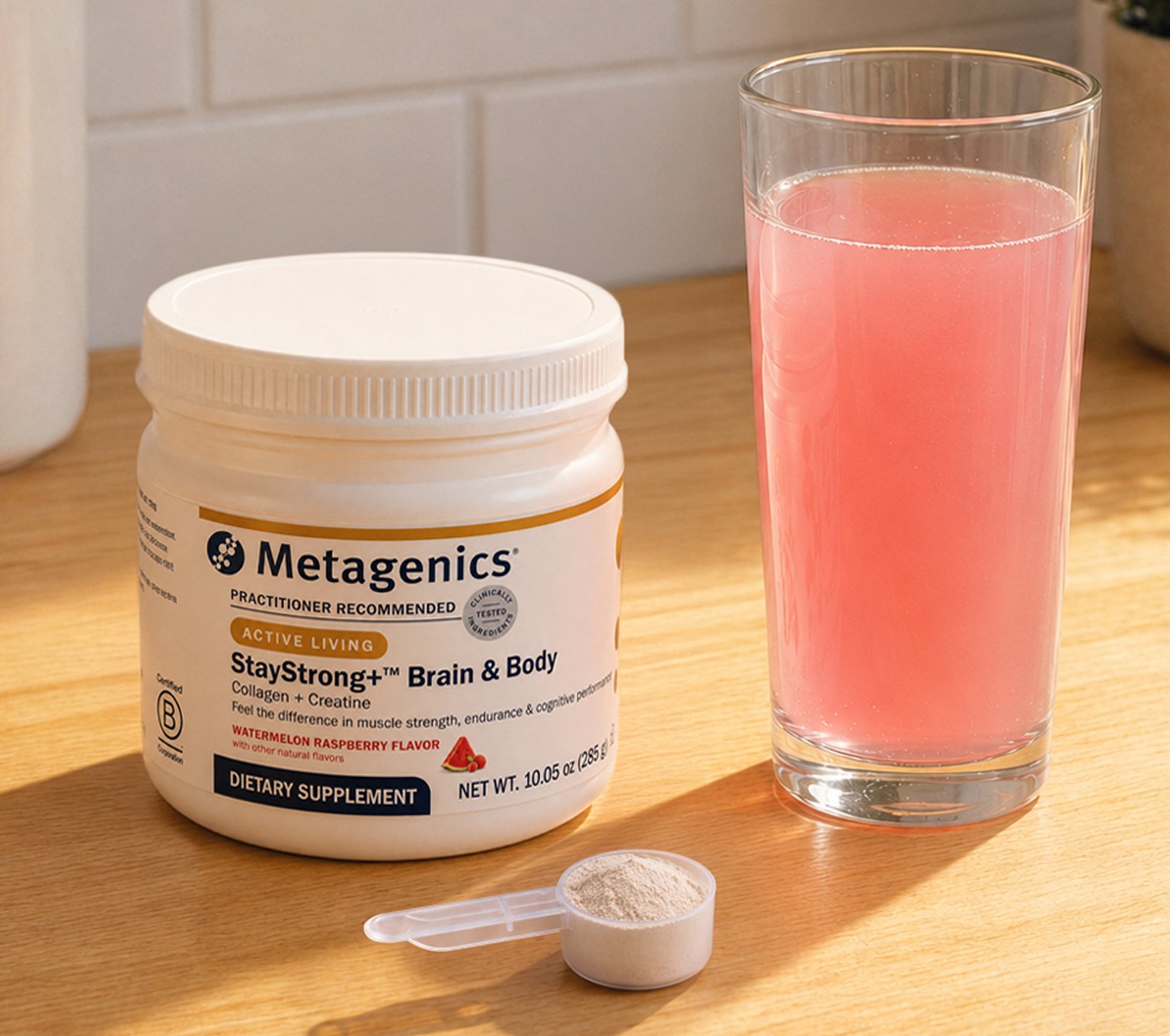 Metagenics® StayStrong™ Brain & Body collagen powder beside a glass of mixed drink, showcasing a daily collagen and creatine supplement.