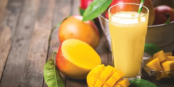 A Mango smoothie in a glass surrounded by freshly sliced mango