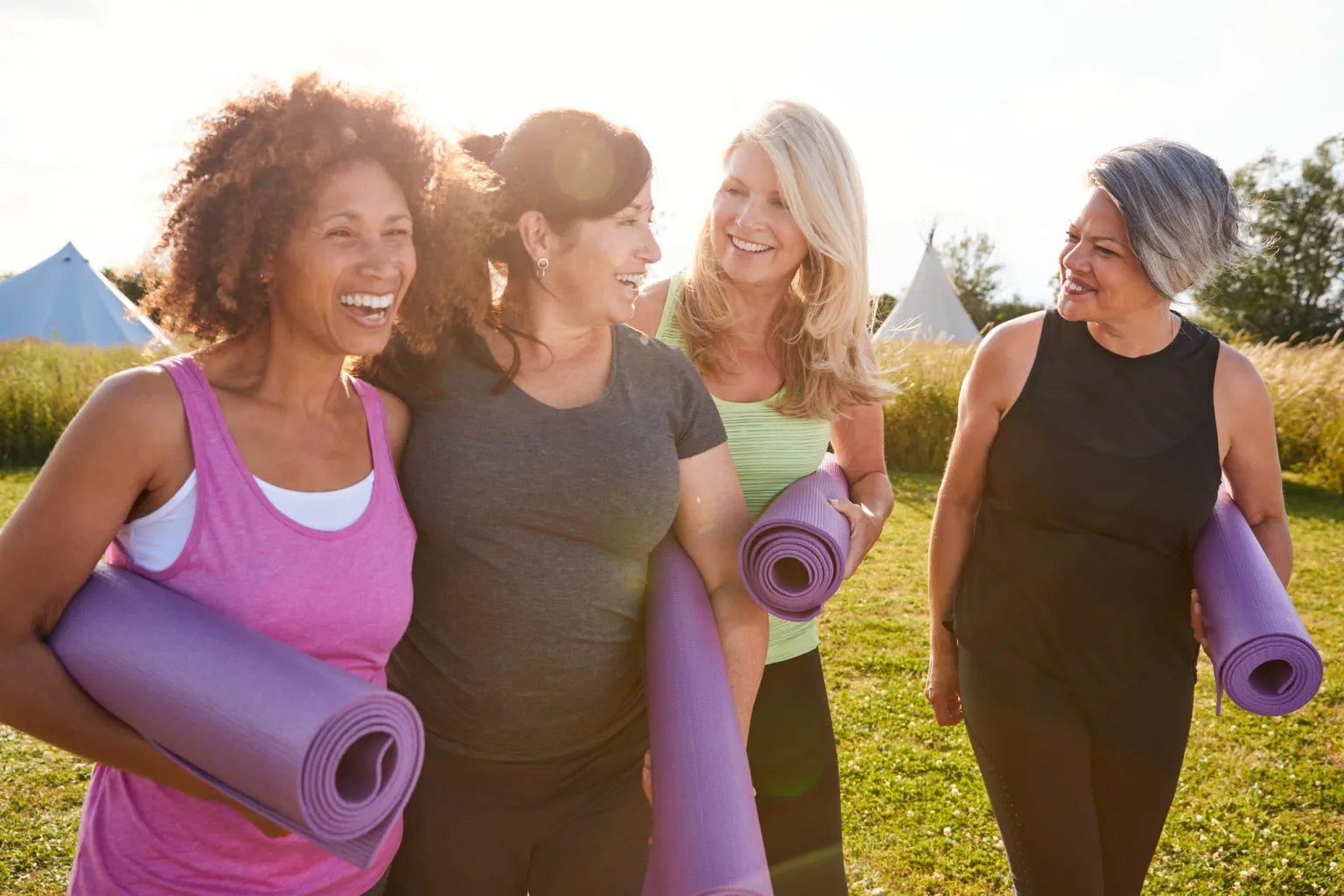 A group of smiling women at an outdoor health retreat carrying yoga mats