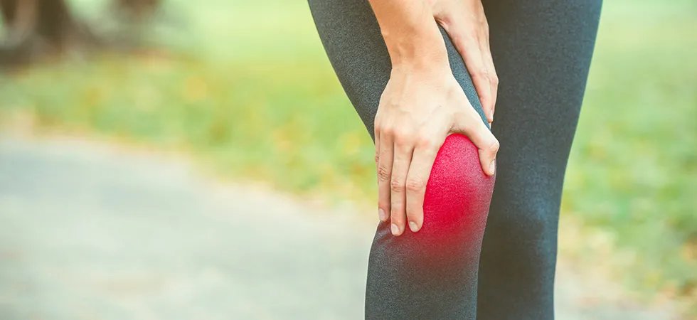 Close up of a woman in exercise leggings clutching her inflamed knee