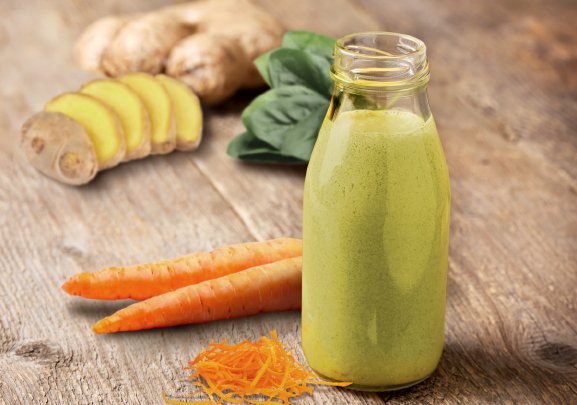 A closeup of a glass bottle with an green colored smoothie with carrots, ginger and spinach
