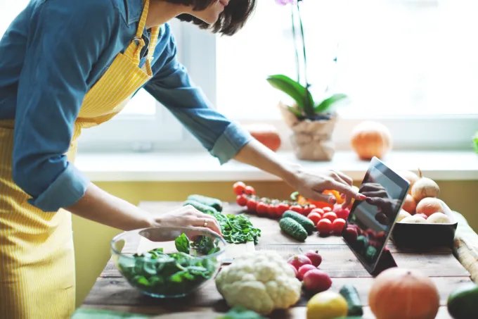 A woman using an tablet while meal prepping with a counter of fresh vegetables