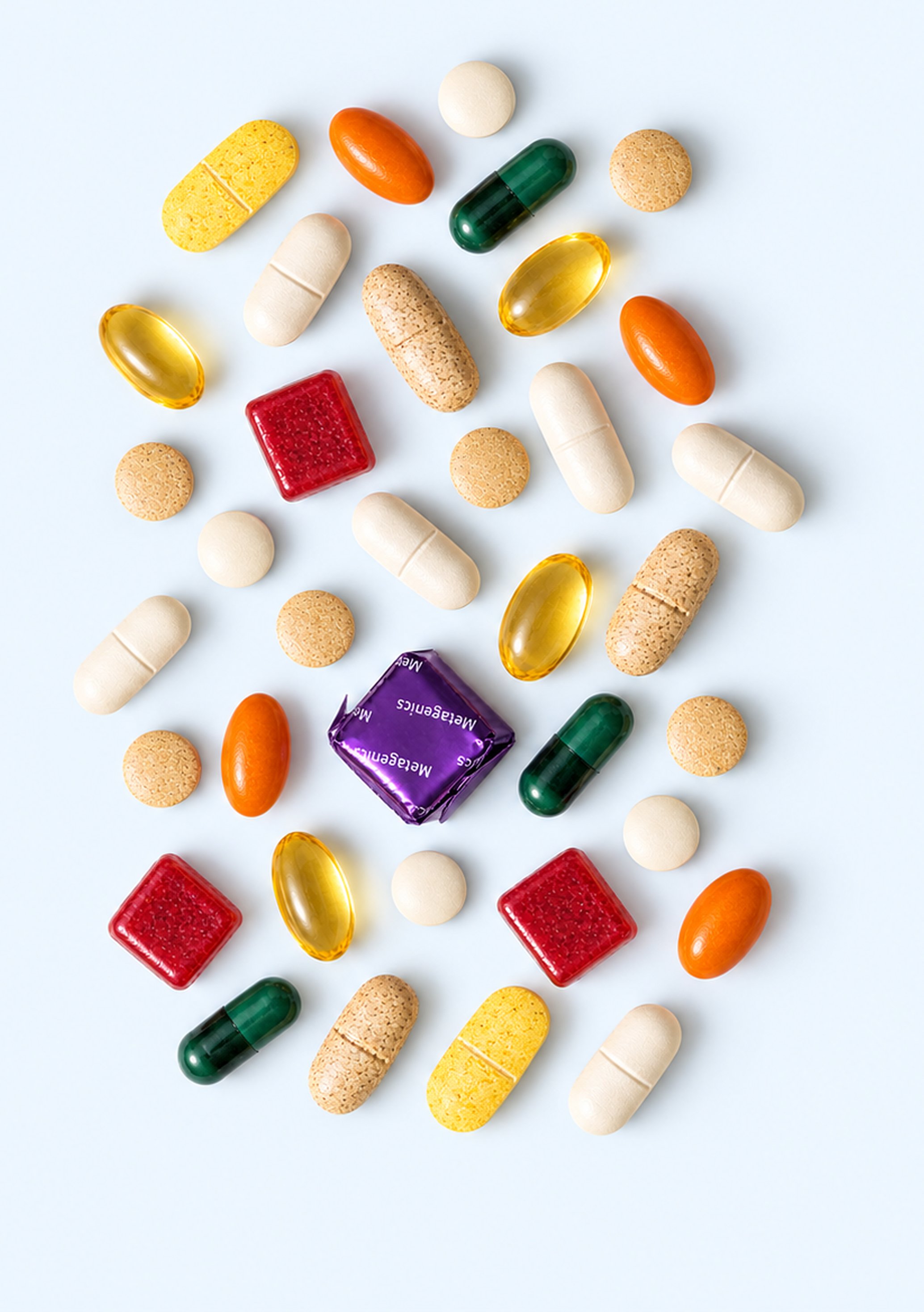 Assortment of colorful Metagenics capsules, tablets, softgels and chews arranged on a light background