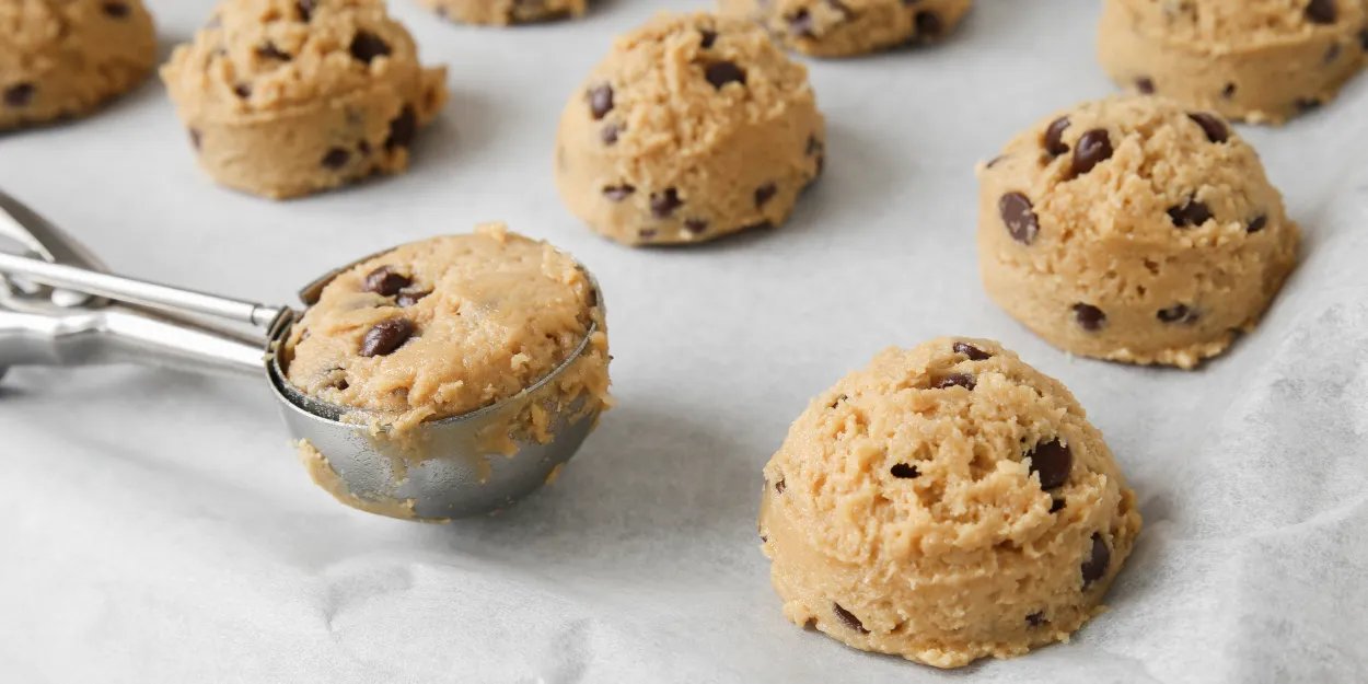 Rows of fat bombs on a parchment lined tray with an ice scream scoop to forming the bombs.