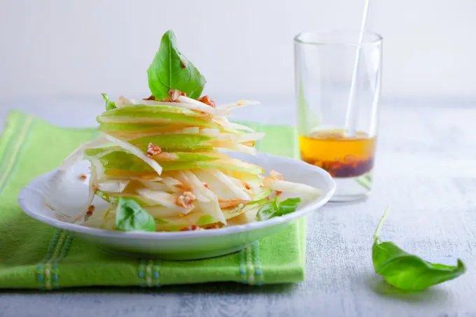 A bowl showing an apple and fennel salad with dressing on the side