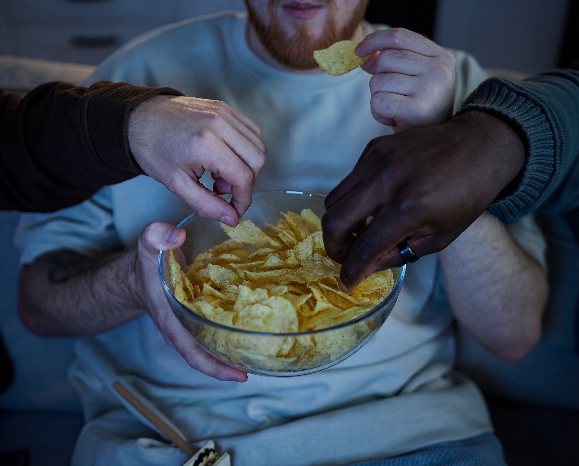 eople reaching into a bowl of chips during a late-night snack, representing how heavy or late meals can disrupt sleep and digestion. Featured on a page about doctor recommended probiotics and lifestyle factors that affect gut health.