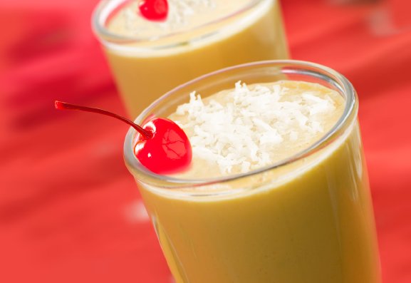 A closeup of a glass with an orange colored smoothie garnished with coconut flakes and a cherry