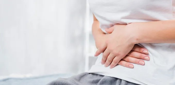 A women sits in a bathroom with her hands pressed against her abdomen.