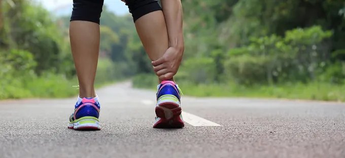 Runner holding their calf on a road, experiencing a leg cramp