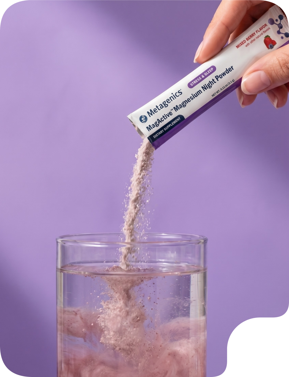Hand pouring Metagenics MagActive® Magnesium Night Powder from a single-serve packet into a glass of water. The powder dissolves into a pink drink against a soft purple background, representing sleep and circadian support.