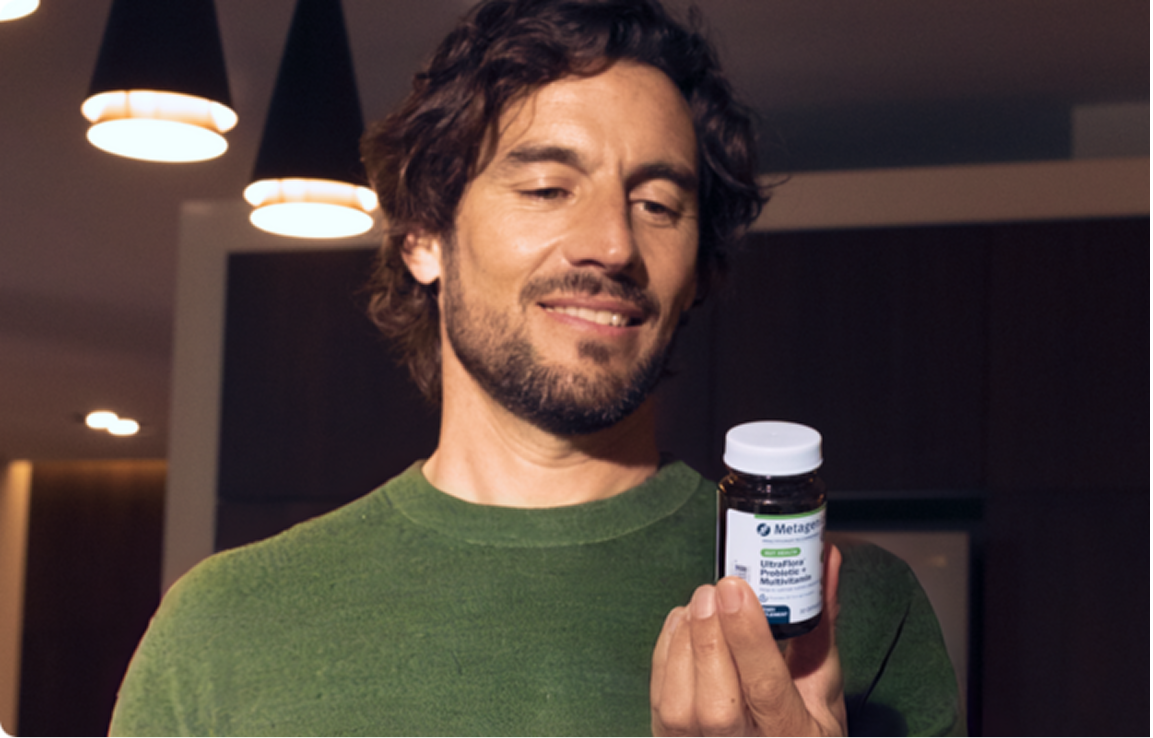 A man wearing a green shirt looks at a bottle of UltraFlora probiotics, reading the supplement facts.