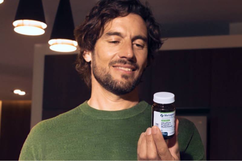 A man wearing a green shirt looks at a bottle of UltraFlora probiotics, reading the supplement facts.