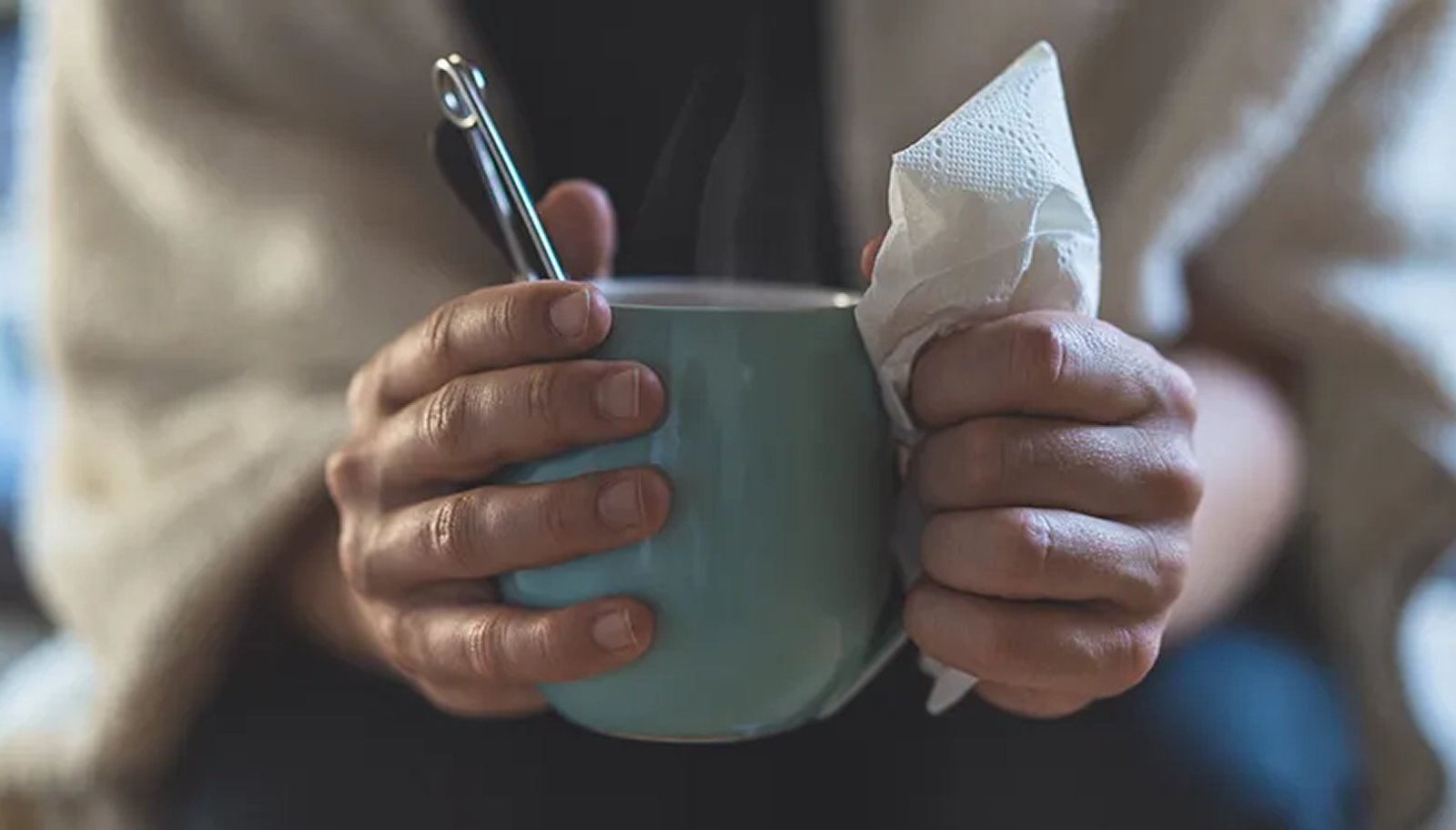 Hands holding a warm drink and tissue, symbolizing immune support during seasonal changes.