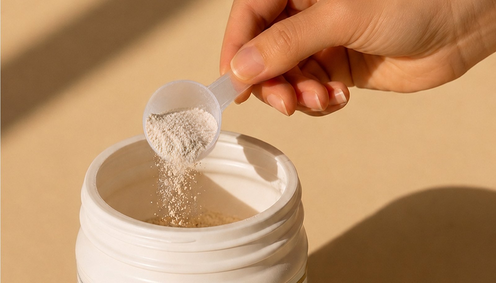 Hand measuring a scoop of collagen powder into a supplement container, illustrating how much collagen per day to take as part of a daily wellness routine.
