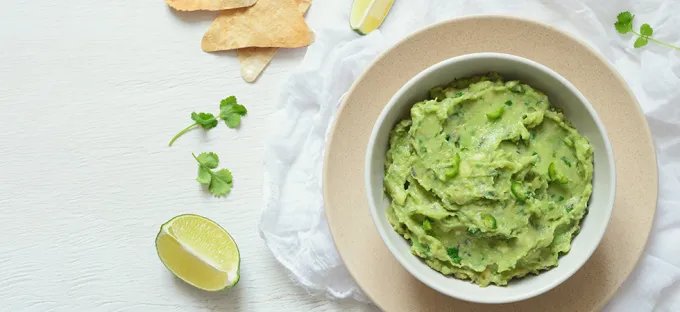 Bowl of guacamole with lime wedges, cilantro, and tortilla chips.