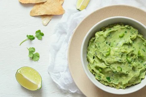 Bowl of guacamole with lime wedges, cilantro, and tortilla chips.