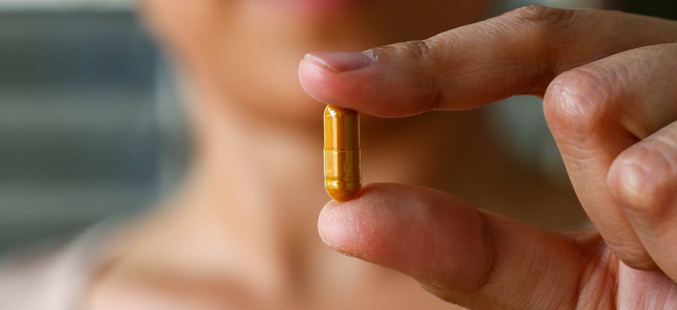 Person holding a dietary supplement capsule between their fingertips.