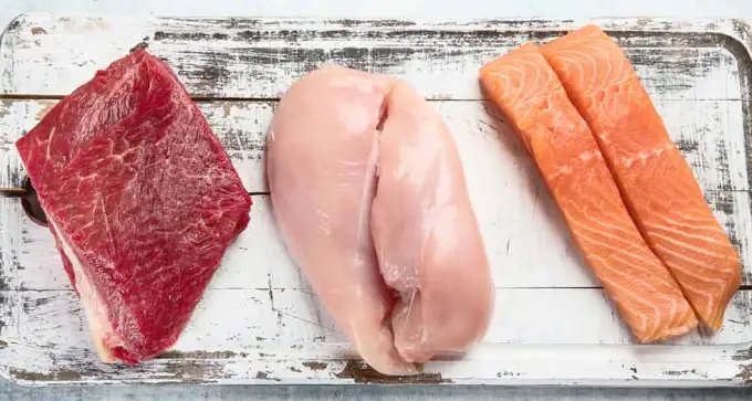 A selection of keto-friendly meats, including steak, chicken breast and salmon on a white cutting board