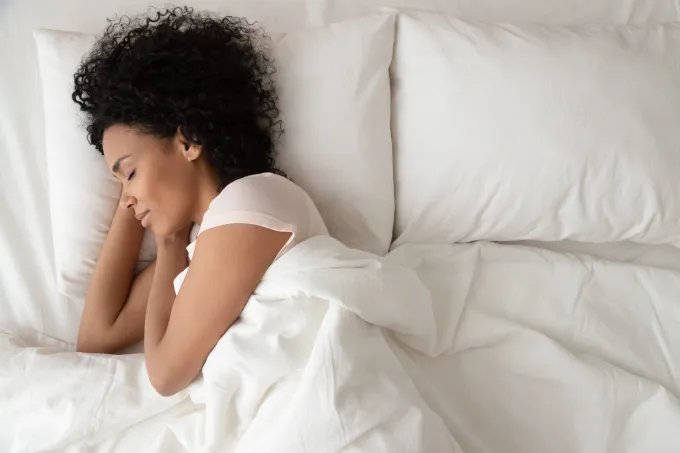 Woman sleeping peacefully in bed, resting on white pillows and wrapped in white bedding.