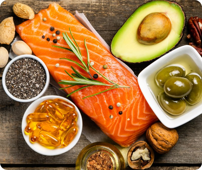 A top-down view of a plate filled with salmon, avocado, olives, nuts, and seeds, displayed on the Metagenics OmegaGenics landing page.