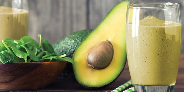 A green smoothie in a glass with half an avocado and a spinach leaves on the table