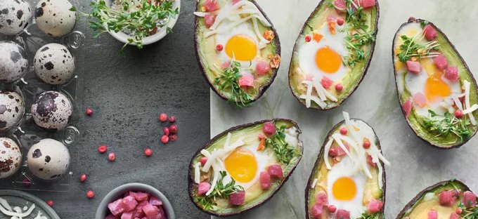 A spread with eggs baked in avocados, with cheese, shopped ham and quail eggs.