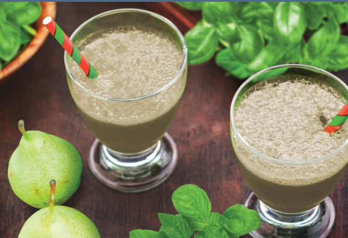 Two glasses of Pear Basil smoothie on a table with fresh bears and basil leaves