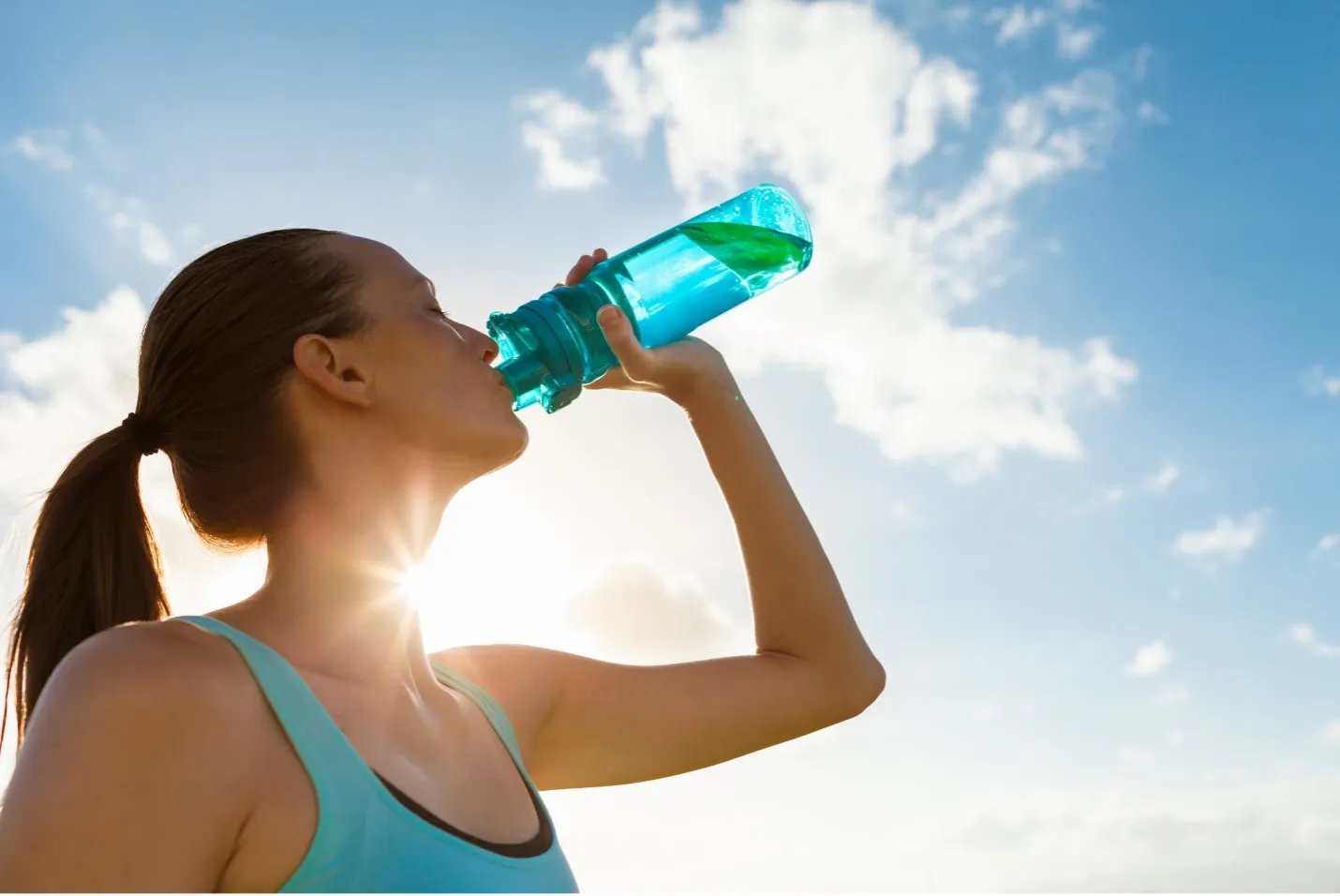 A woman in exercise gear dinks from her water bottle against a blue sky