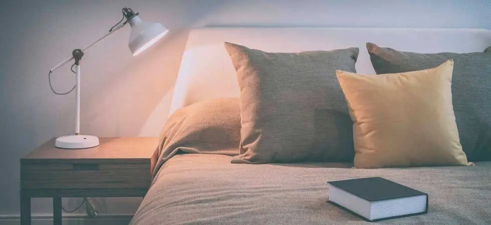 A comfortable bed with a bedside table, lamp and a book