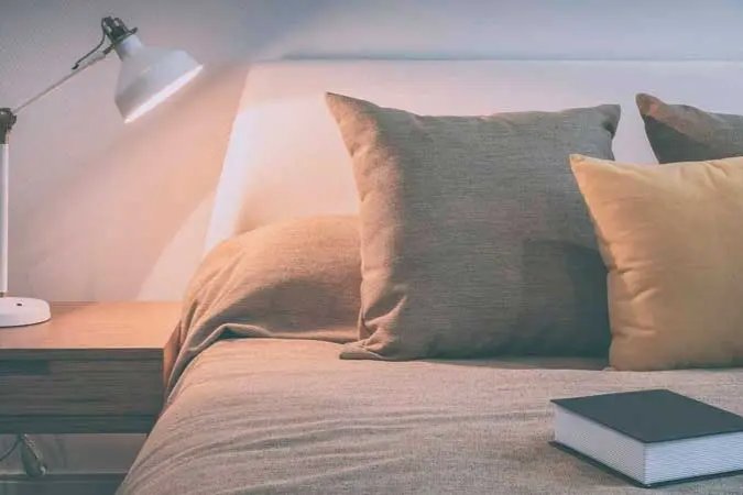 A comfortable bed with a bedside table, lamp and a book