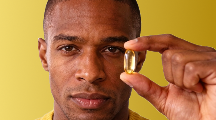 A close-up of a person holding a single softgel capsule between their fingers against a yellow background, shown on the Metagenics OmegaGenics® landing page hero banner.