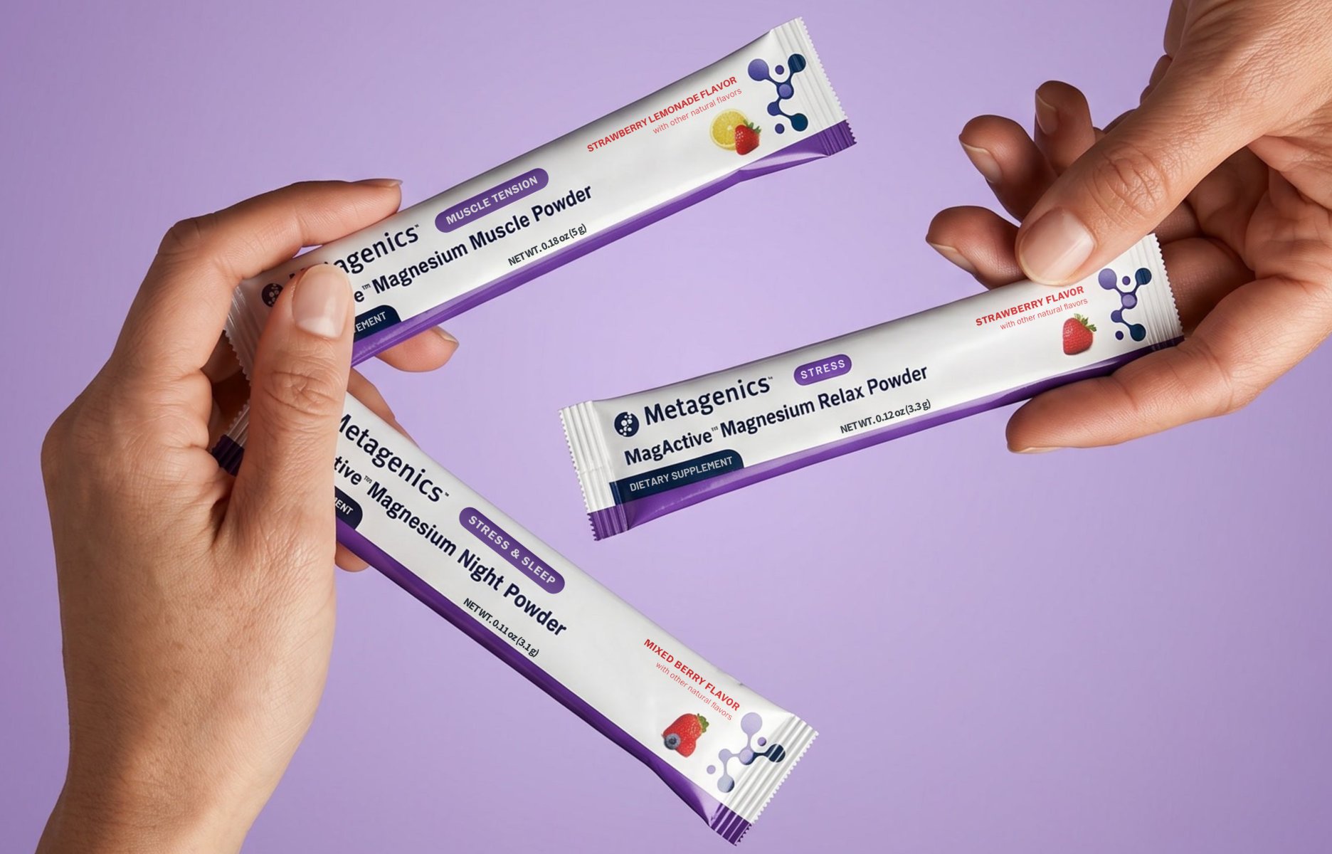 Hands holding three individually packages of Metagenics' MagActive magnesium powder supplements against a light purple background.